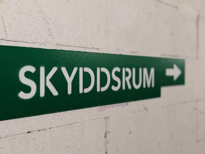 en grön skylt på en betongvägg. På skylten står det "skyddsrum"